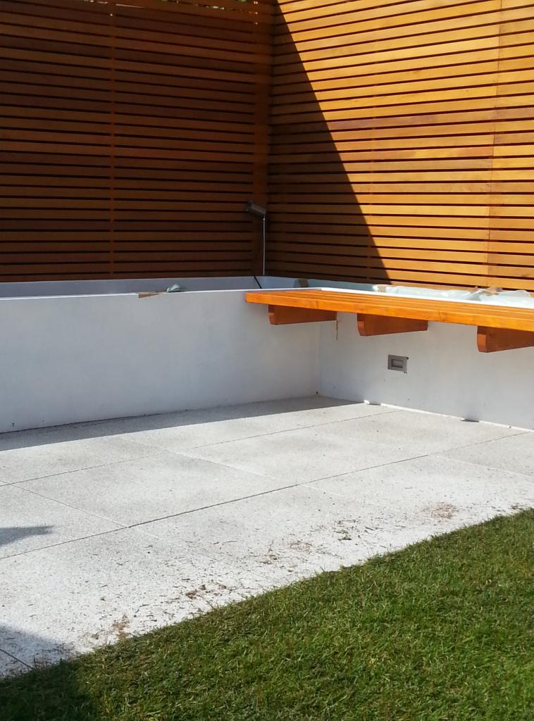 Nowoczesny taras w Tarnowie z drewnianą zabudową i siedziskiem, wykończony jasną kostką brukową i fragmentem trawnika.