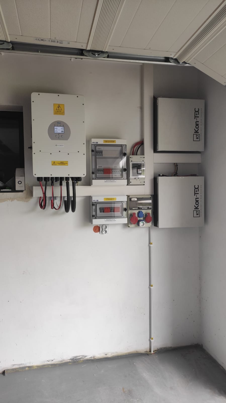 Kompletna instalacja fotowoltaiczna w pomieszczeniu: inwerter, rozdzielnice, akumulatory Kon-TEC. Widoczne okablowanie i zabezpieczenia. Gotowy system OZE.