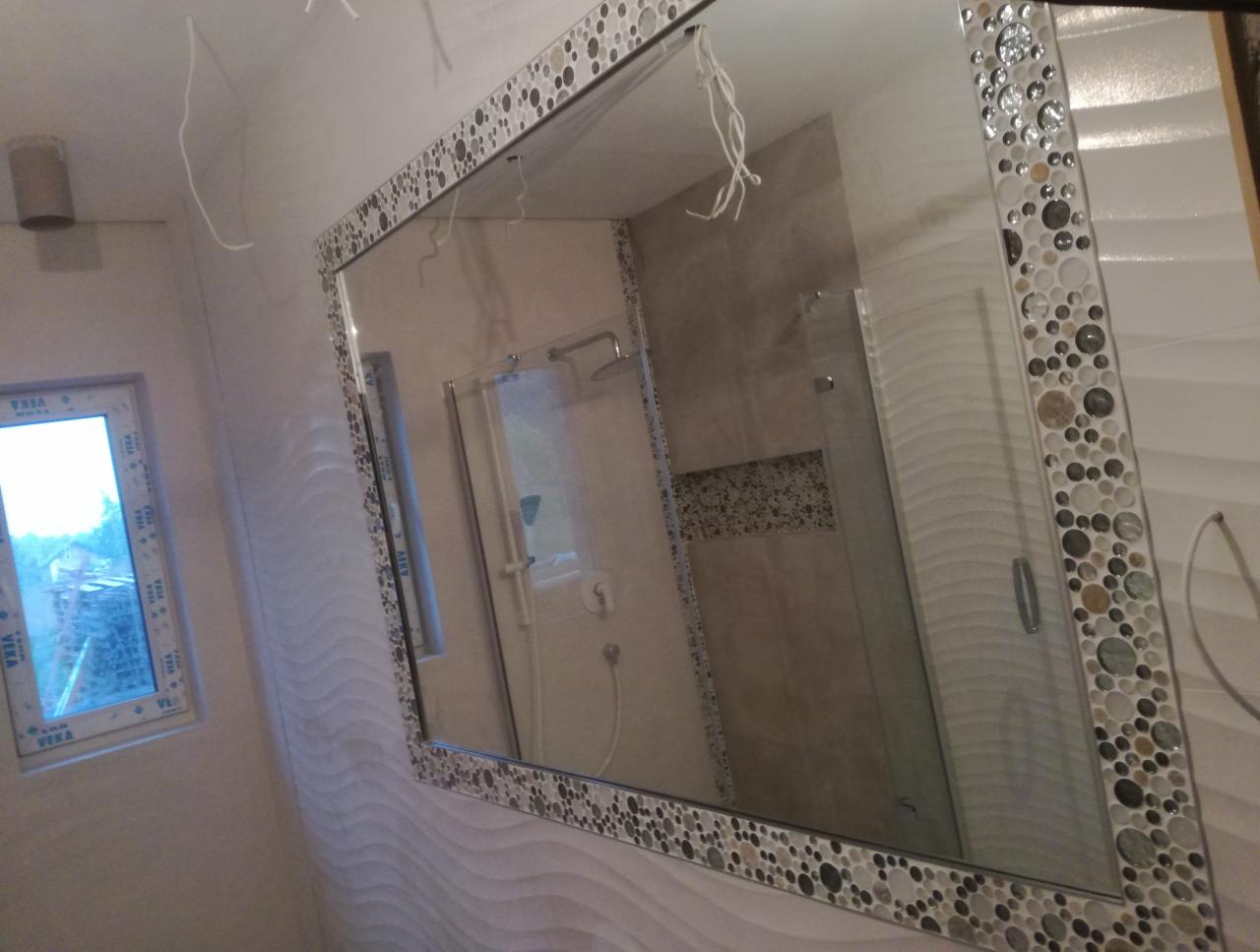 Nowoczesna łazienka z lustrem w ozdobnej ramie z motywem kamieni, widok na kabinę prysznicową i okno z widokiem na zewnątrz.