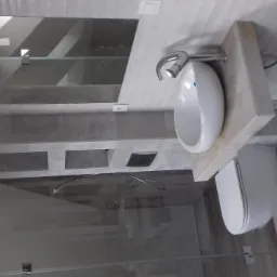 Nowoczesna łazienka z szarą, płytkową okładziną, wiszącą białą umywalką na drewnianym blacie, podwieszaną toaletą i przeszkloną kabiną prysznicową.