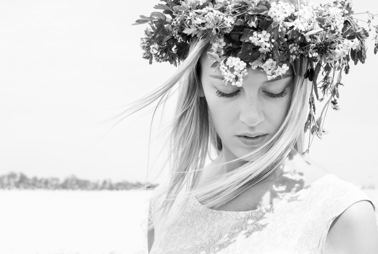 Portret kobiety z długimi blond włosami i wiankiem z białych kwiatów na głowie, czarno-białe zdjęcie z delikatnym tłem.