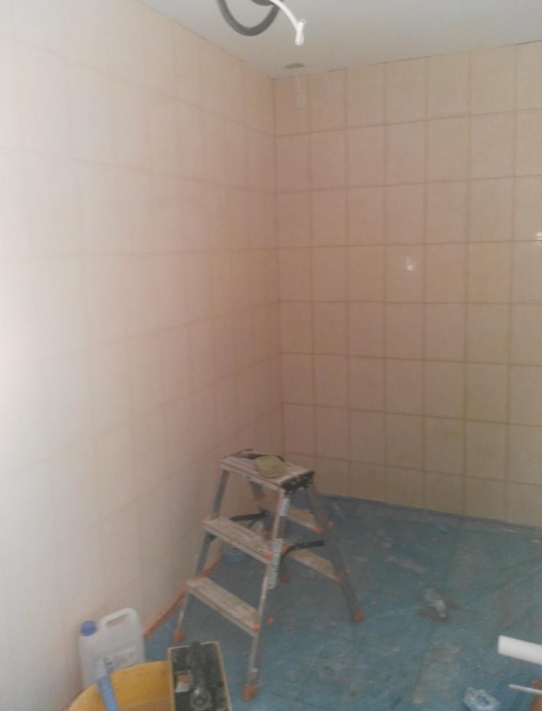 Ściany w trakcie remontu w Michałowie, wyłożone jasnymi płytkami, zabezpieczona podłoga, drabina i wiadro z narzędziami w rogu pomieszczenia.