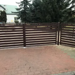 Brązowa, nowoczesna brama przesuwna z poziomymi panelami, zamontowana na posesji z kostką brukową i widokiem na dom oraz drzewa.