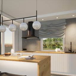Simple Form Renia Bartoszek - Nowoczesna kuchnia z wyspą o drewnianym blacie, okrągłymi lampami i dekoracyjną roletą rzymską. Widok na zieleń za oknem i czarne zasłony po lewej stronie.