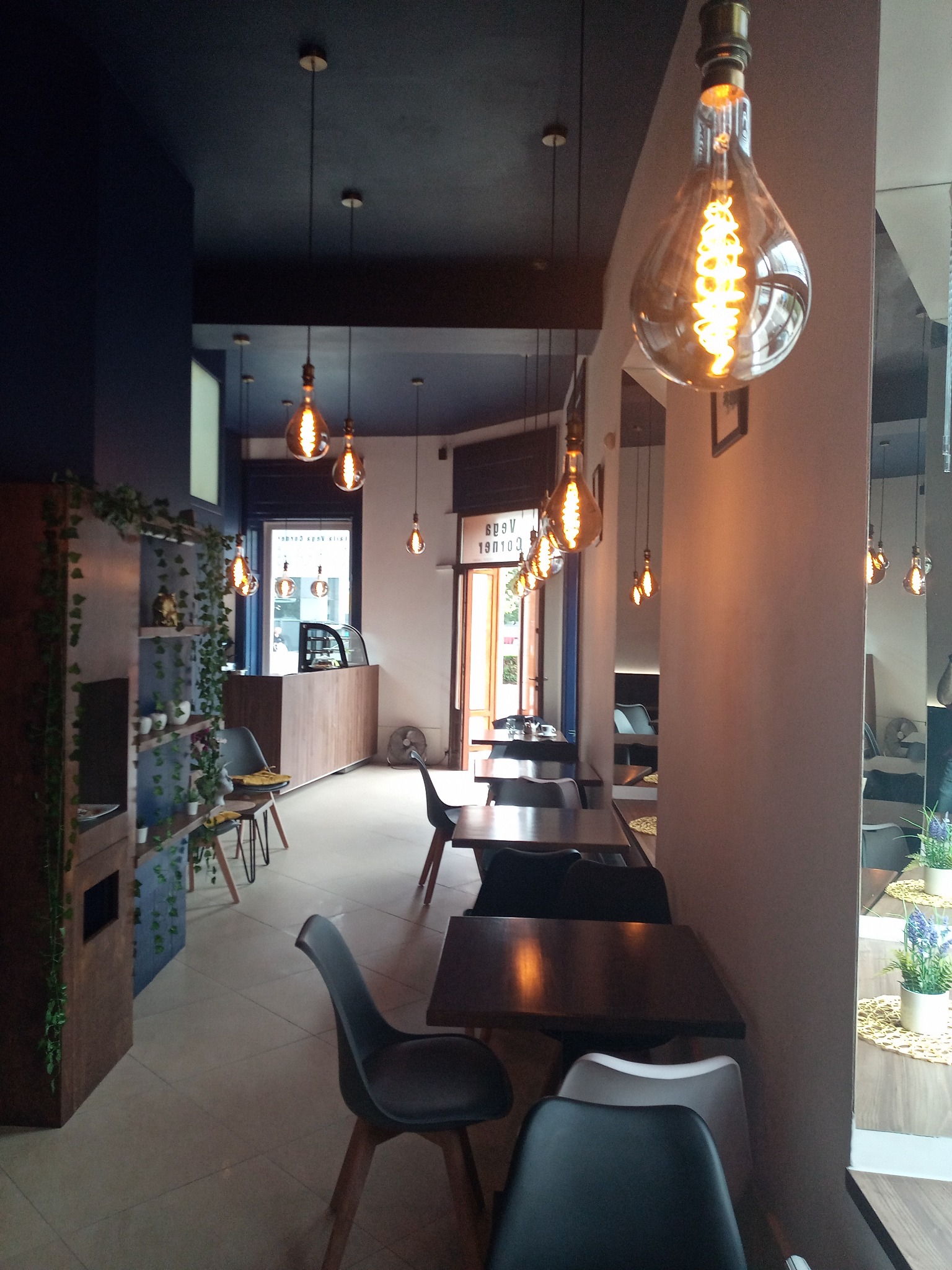 Wnętrze kawiarni z ciemnymi ścianami, drewnianymi stolikami i krzesłami, oświetlone dekoracyjnymi żarówkami Edison