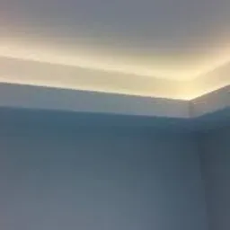 Minimalistyczne wykończenie sufitu z ukrytym oświetleniem LED, tworzące efekt subtelnej poświaty na ścianach. Widoczny narożnik pomieszczenia z równo pomalowanymi powierzchniami.