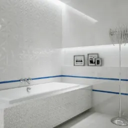 Nowoczesna łazienka w bieli z akcentami błękitu, dekoracyjna ściana z tr&oacute;jwymiarowych płytek, wanna obudowana płytkami z motywem fal, chromowany wieszak na ręczniki i ramki ze zdjęciami...