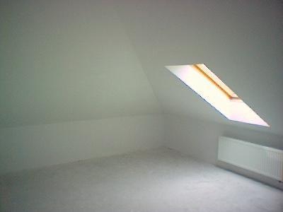 Poddasze po remoncie: świeżo pomalowane ściany na biało, widoczne okno dachowe i grzejnik, surowy beton na podłodze.