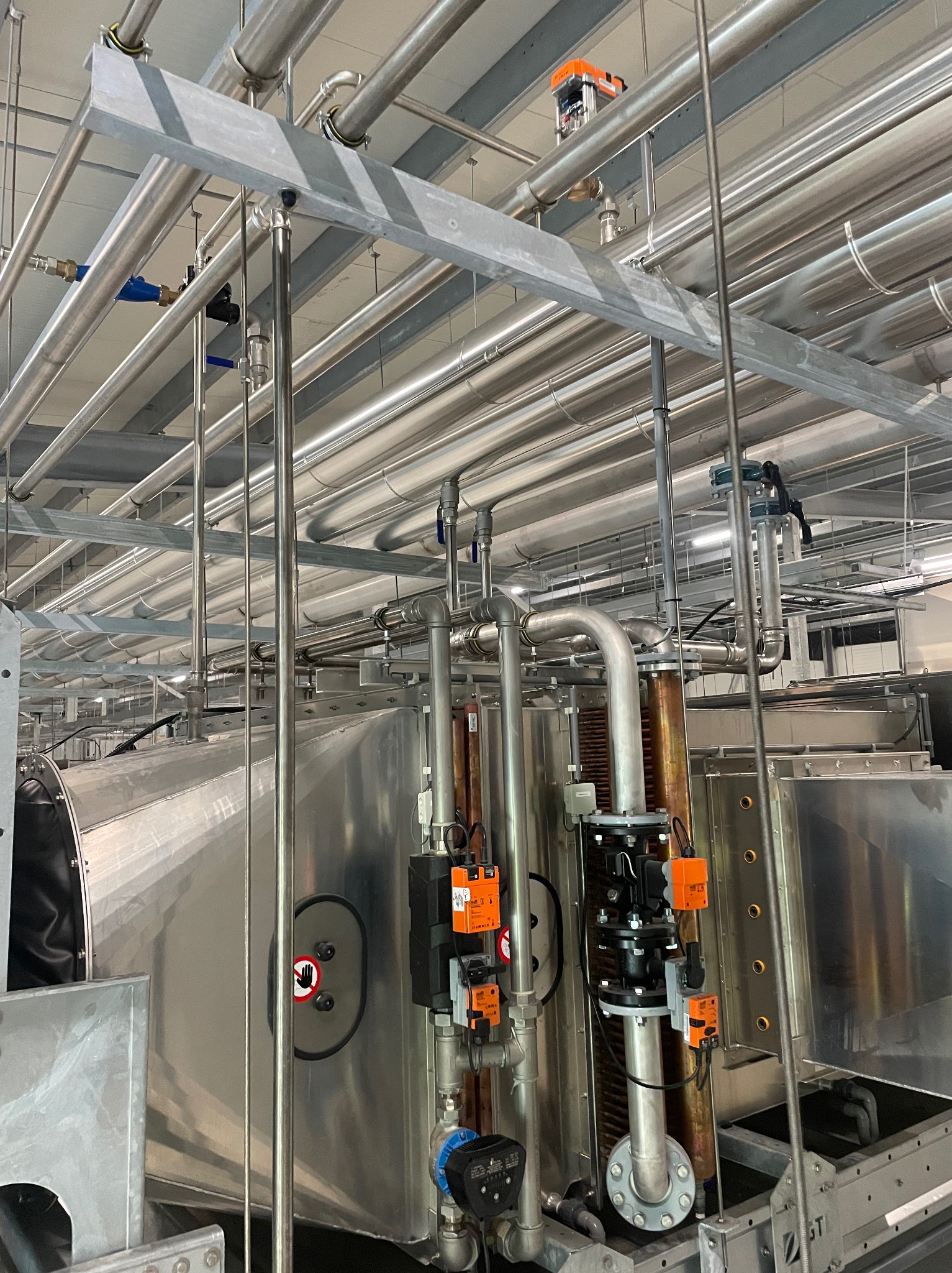 Kompleksowa instalacja rur wentylacyjnych i hydraulicznych w budynku przemysłowym, widoczne liczne rury ze stali nierdzewnej, zawory, czujniki oraz elementy mocujące.