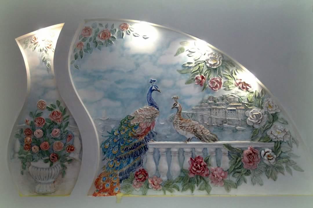 Dekoracyjna płaskorzeźba ścienna z motywem pawi, kwiatów i pejzażu miejskiego, wykonana w technice sztukaterii, oświetlona od góry.