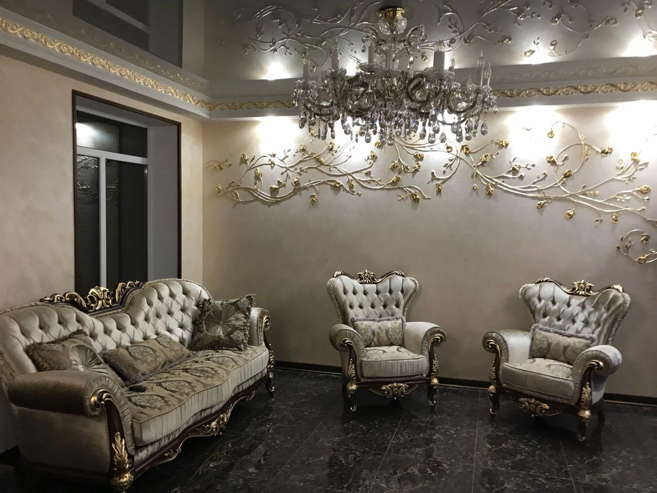 Elegancki salon z dekoracyjną sztukaterią na ścianie imitującą pnącze z drobnymi, złotymi kwiatami, kryształowy żyrandol, marmurowa podłoga i klasyczne meble tapicerowane w jasnych kolorach...
