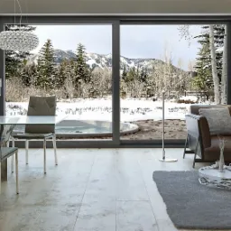 Nowoczesny salon z przesuwnymi drzwiami tarasowymi, widok na zimowy krajobraz z zewnątrz, w tle ośnieżone góry i drzewa.