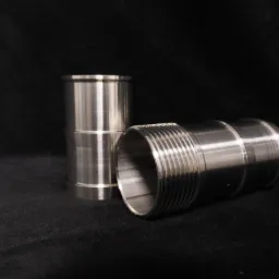 Dwa metalowe elementy cylindryczne, jeden pionowo, drugi poziomo z gwintem, na czarnym tle.