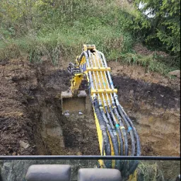 Żółta koparka w trakcie prac ziemnych w Krzczonowie, widok z kabiny operatora na wykop pod instalacje.