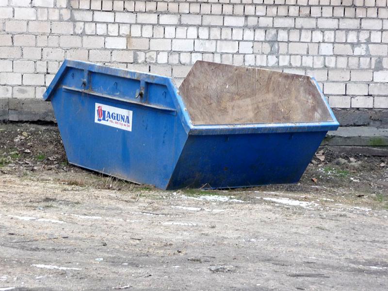 Niebieski kontener na gruz z logo firmy Maguna, stojący na ziemi przed murem z białej cegły w Gorzowie Wielkopolskim.