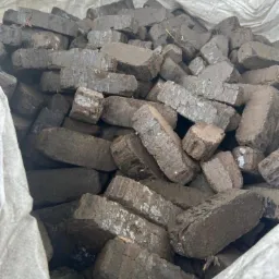 Stos ciemnych, prostokątnych brykietów drzewnych w worku jutowym, oferowanych przez firmę z Gdańska. Widoczne nierówności i naturalna struktura materiału.