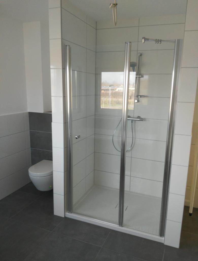 Nowoczesna kabina prysznicowa z widokiem na zewnątrz przez okno, białe płytki ścienne i szare podłogowe, kompaktowa toaleta w rogu