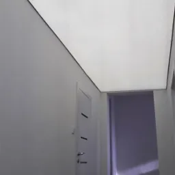 Biały sufit napinany z czarnym obramowaniem w przedpokoju z drewnianymi schodami i białą ścianą z drzwiami.