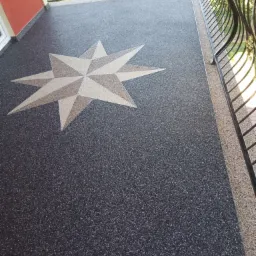 Szara posadzka na balkonie z wzorem gwiazdy w odcieniach beżu i brązu, widok z góry, czarna metalowa balustrada w tle.