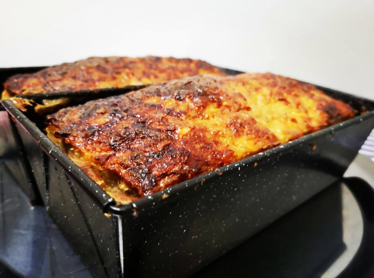 Dwie formy pieczonego pasztetu z chrupiącą, przypieczoną skórką, umieszczone na czarnym, błyszczącym talerzu.