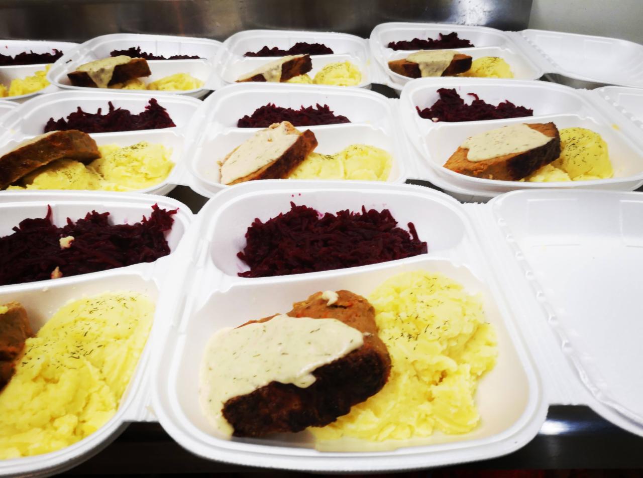 Porcje obiadowe w białych, plastikowych pojemnikach: kotlet mielony z sosem koperkowym, ziemniaki puree posypane koperkiem i buraczki. Przygotowane do transportu.