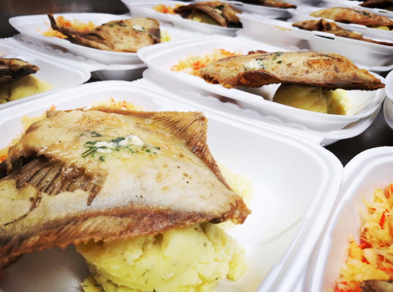 Porcje smażonej ryby z ziemniakami i surówką w białych, styropianowych opakowaniach na wynos, widoczne z góry.