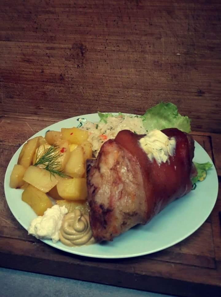 Pieczona golonka z ziemniakami, kapustą i sosem na jasnoniebieskim talerzu, rustykalne drewniane tło.