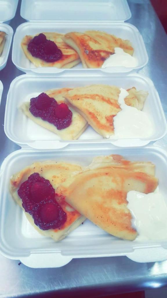 Pojemniki styropianowe z naleśnikami, dżemem malinowym i kleksem śmietany, ułożone jeden na drugim.