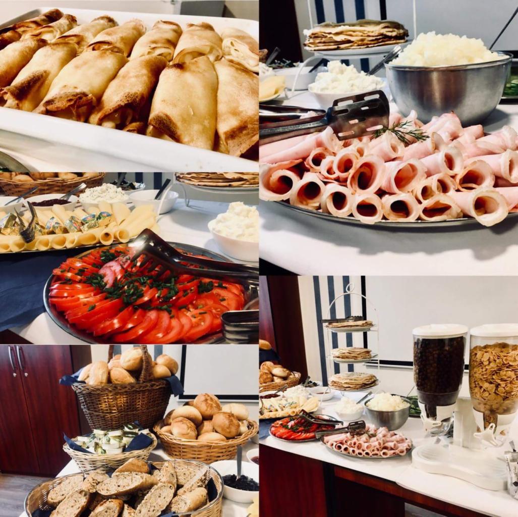 Bogato zastawiony stół szwedzki z roladkami naleśnikowymi, wędlinami, serami, pomidorami, pieczywem w koszykach oraz płatkami śniadaniowymi w dyspenserach, idealny na imprezę firmową.