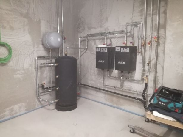 Kompleksowa instalacja podgrzewania wody użytkowej z dwoma wymiennikami ciepła KTS i buforem 500 litrów, wykonana ze stali nierdzewnej w systemie zaciskanym, widoczna na tle surowych ścian...