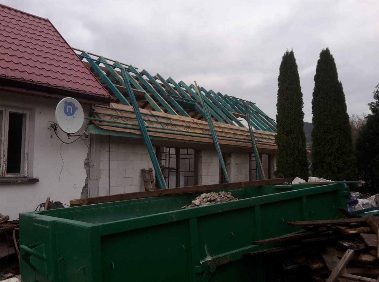 Dom w trakcie remontu w Limanowej, widoczna konstrukcja dachu z drewnianymi belkami, kontener na gruz i elewacja z białego bloczka.