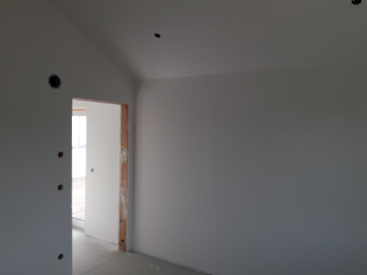 Wnętrze pokoju w trakcie wykańczania: ściany pomalowane na szaro, widoczne otwory na instalacje elektryczne, białe drzwi z surową ościeżnicą.