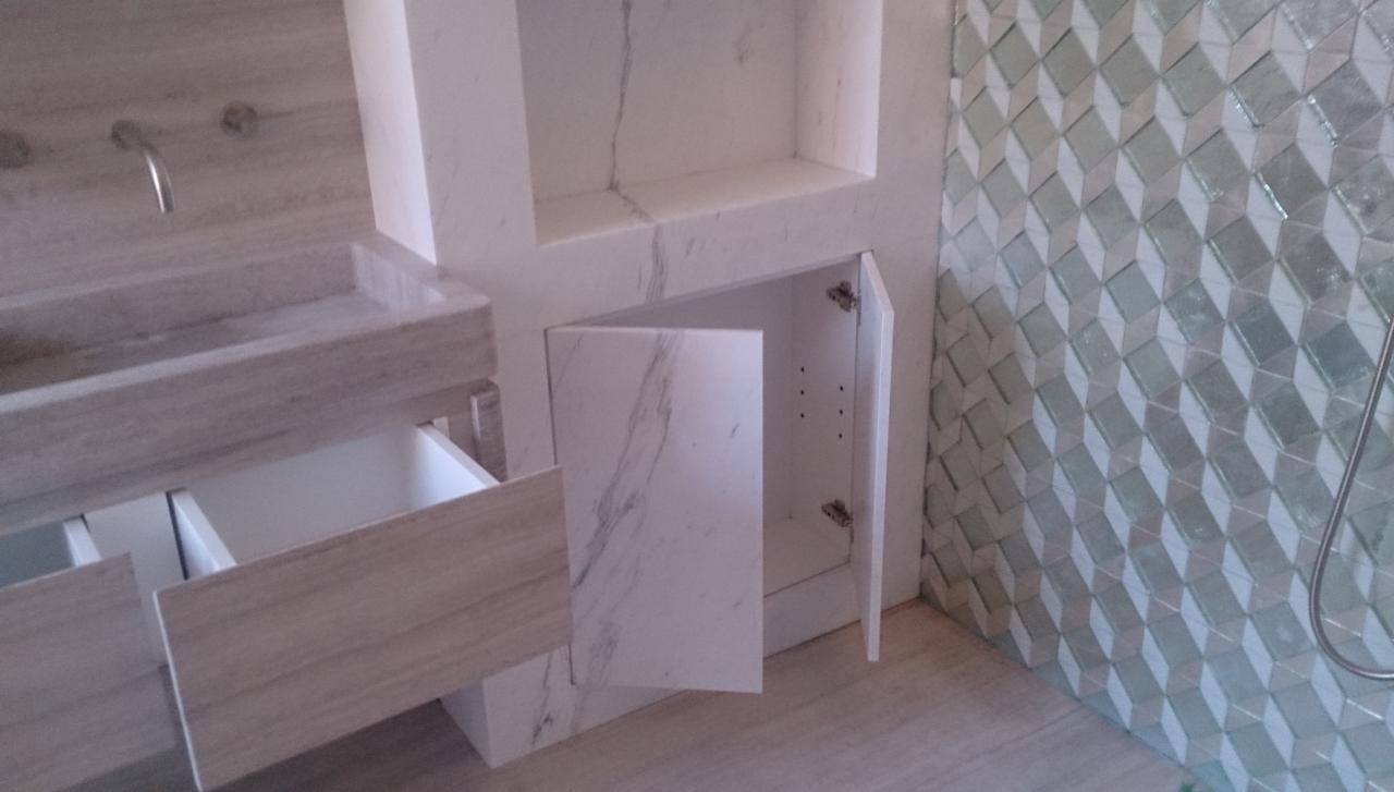 Nowoczesna łazienka z umywalką z szarego kamienia z otwartą szufladą, szafką z marmurowymi drzwiczkami i ścianą wyłożoną trójwymiarowymi kafelkami w odcieniach bieli i zieleni.