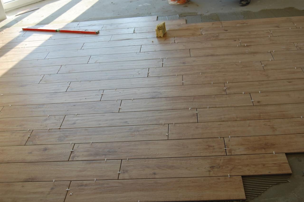 Układanie podłogi z płytek imitujących drewno, widoczne krzyżyki dystansowe, poziomica i gąbka do czyszczenia fug.