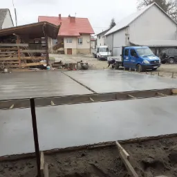 Wylana, świeża posadzka przemysłowa z drewnianym szalunkiem. W tle budynki gospodarcze, domy i pracownik przy samochodzie firmowym.