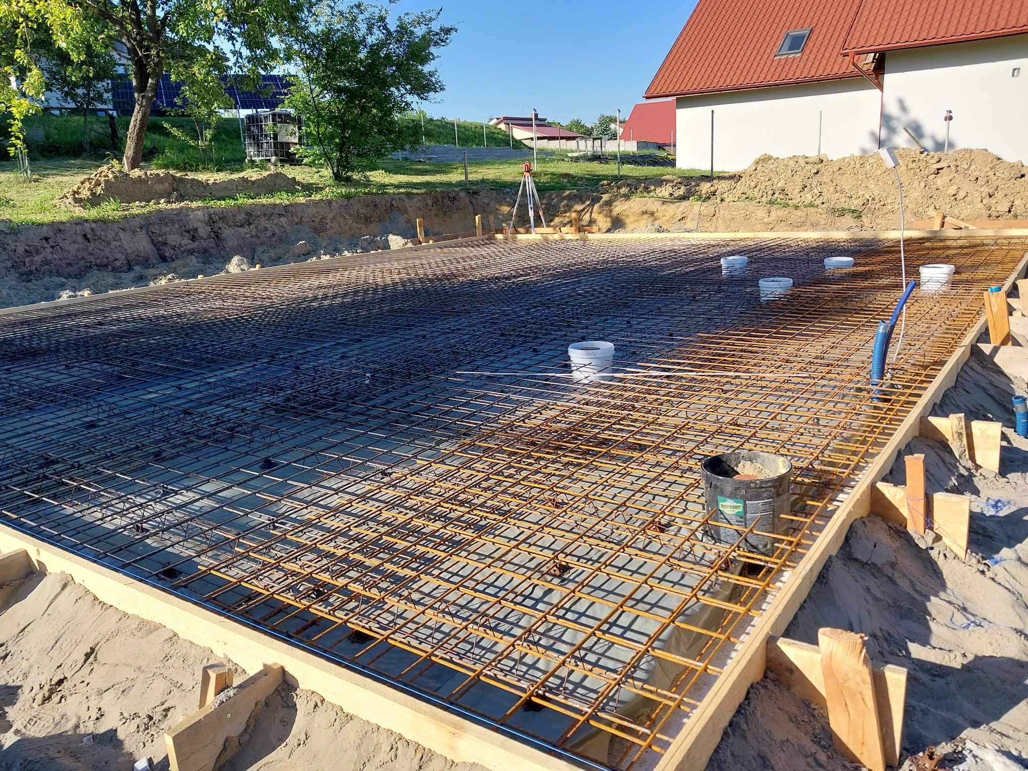 Zbrojenie fundamentów domu jednorodzinnego, widoczne deskowanie i poziomica laserowa w tle, przygotowanie do wylania betonu.