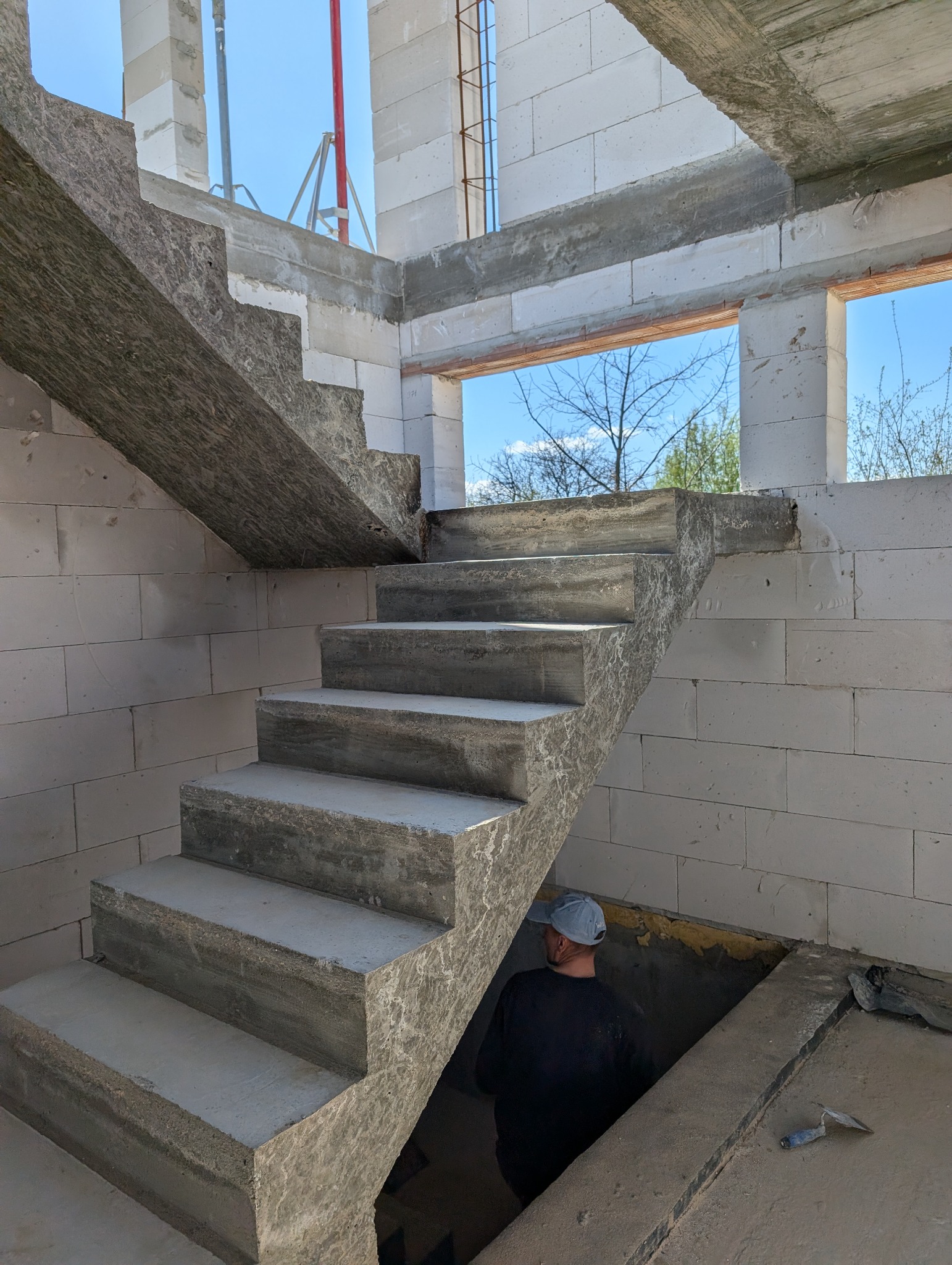Surowe, betonowe schody wewnętrzne w trakcie budowy domu z bloczków, widoczny pracownik i kielnia.