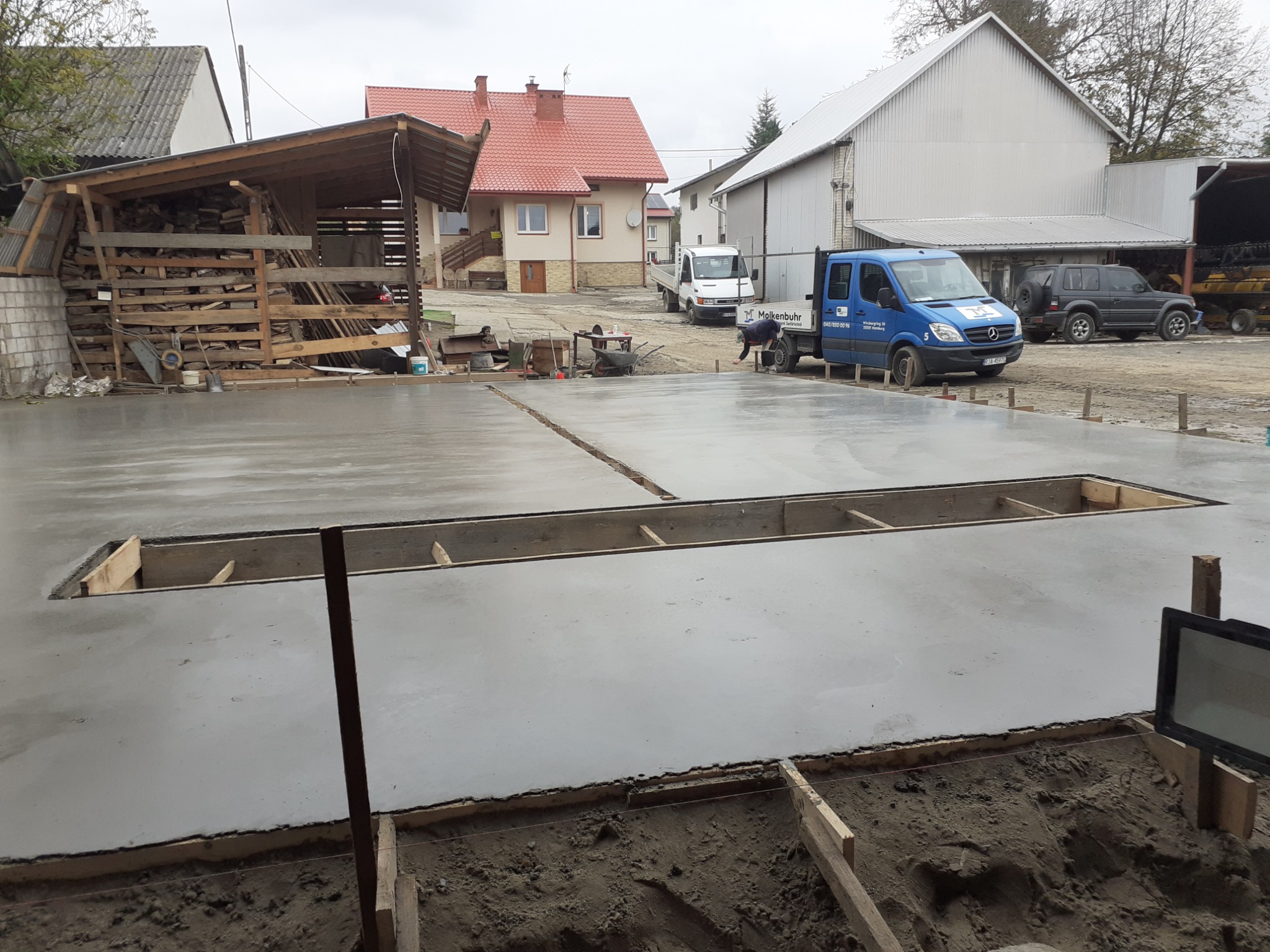 Wylana, świeża posadzka przemysłowa z drewnianym szalunkiem. W tle budynki gospodarcze, domy i pracownik przy samochodzie firmowym.