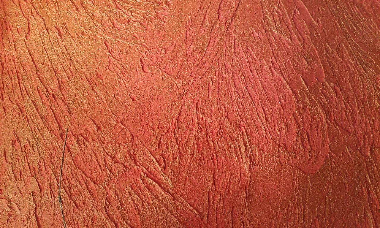 Pomarańczowo-czerwona ściana z wyraźną, teksturowaną fakturą, przypominającą ślady pędzla lub szpachli, z delikatnym połyskiem.
