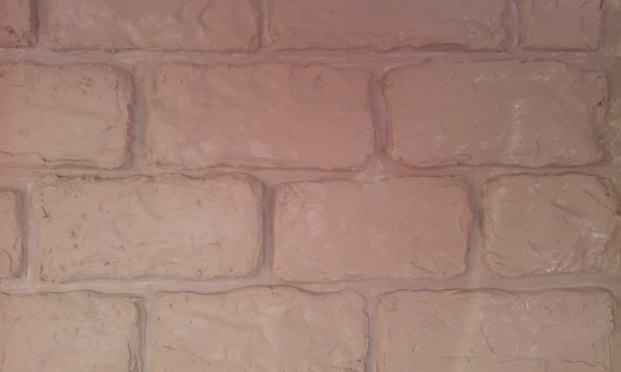 Fragment ściany z efektem dekoracyjnym imitującym cegły w odcieniach beżu i bieli, z widoczną fakturą i nierównościami.