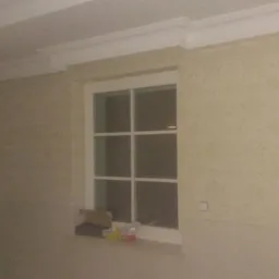 Pokój po remoncie z tapetą w delikatny wzór, biała stolarka okienna z pudełkiem i puszką farby na parapecie, widoczne listwy przysufitowe.