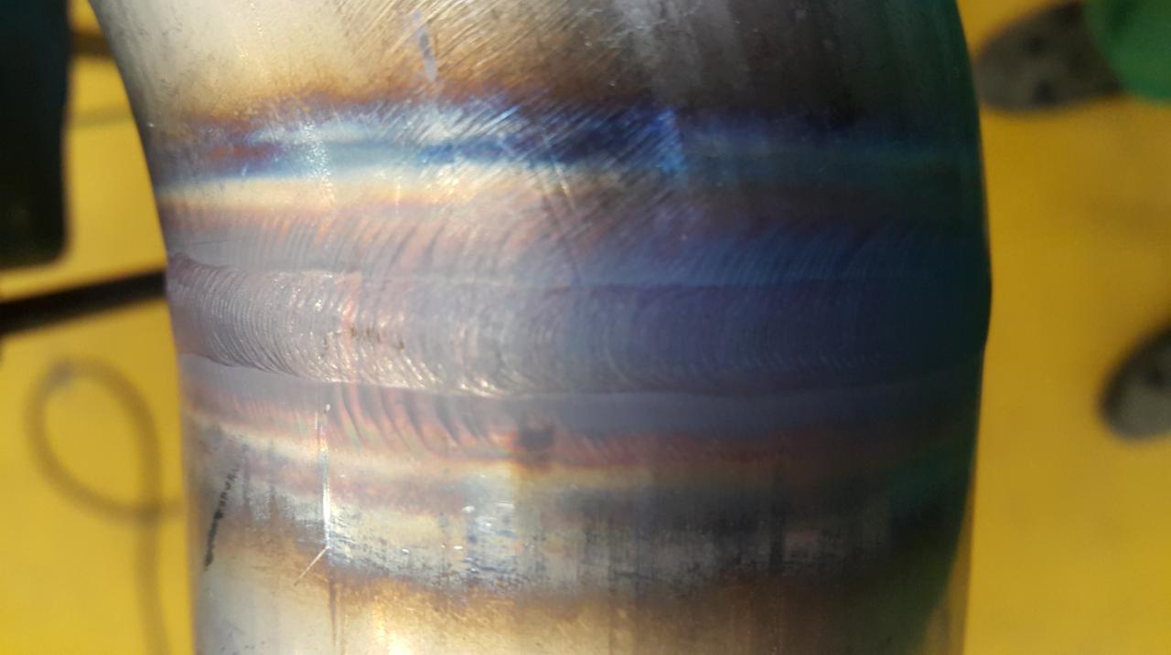 Szczegółowe zbliżenie spoiny na rurze ze stali nierdzewnej, widoczne charakterystyczne przebarwienia termiczne i ślady obróbki.