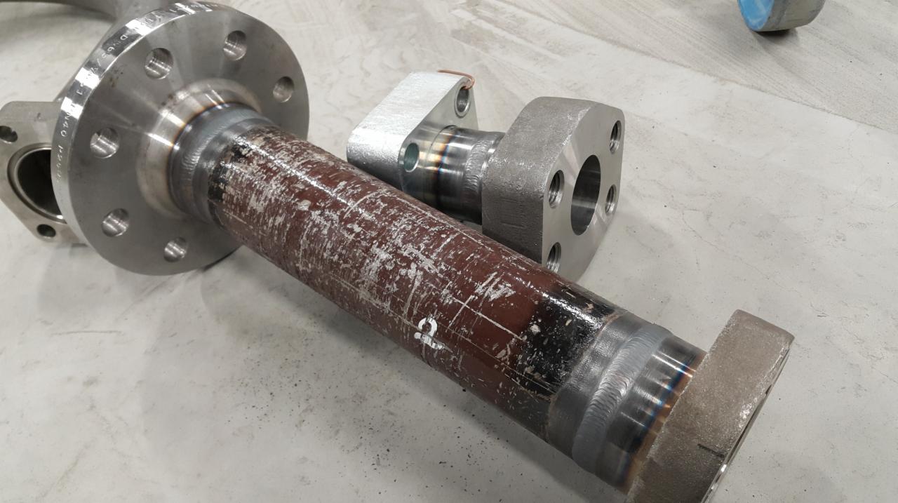 Elementy rurociągów ze stali nierdzewnej połączone spawami, widoczne ślady obróbki i czyszczenia powierzchni, flansze z otworami na śruby.