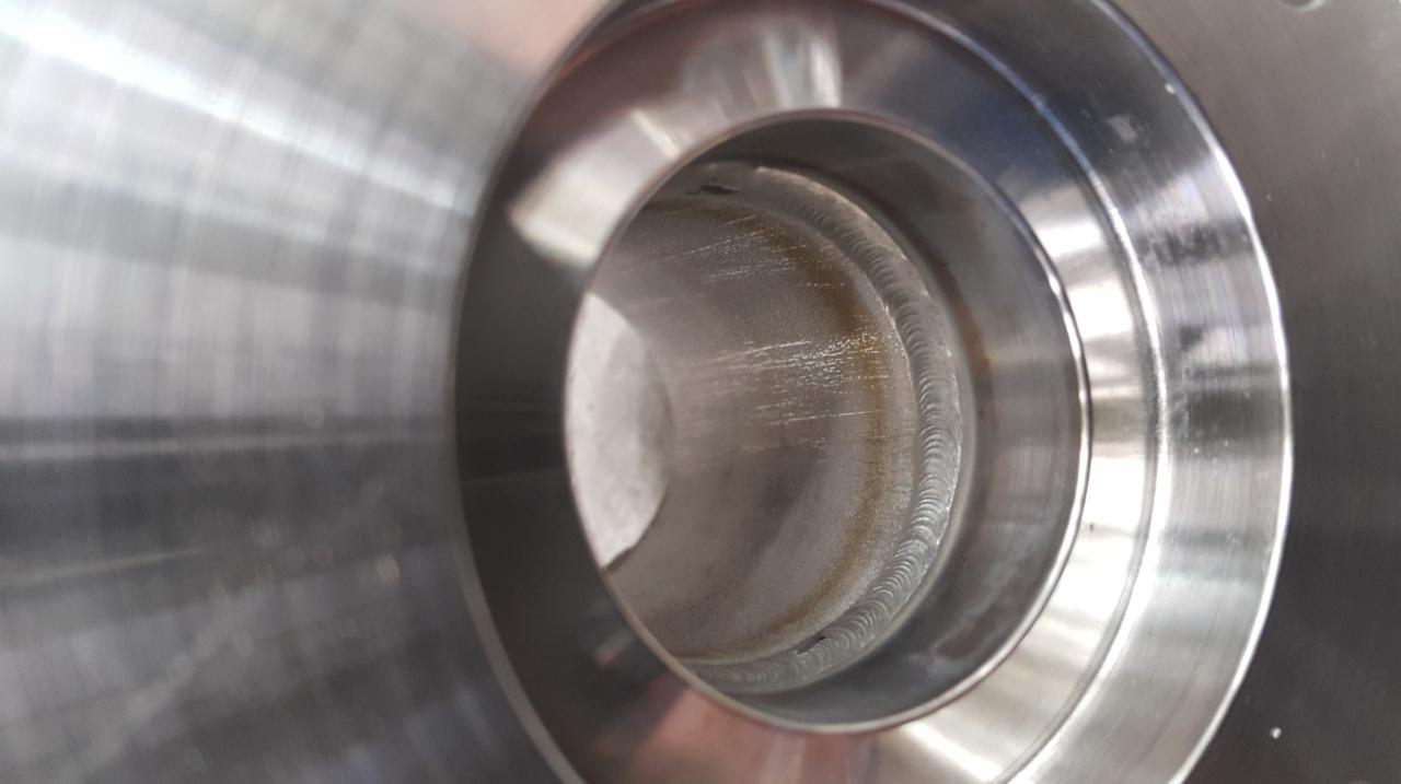 Wewnętrzny widok spawu wewnątrz metalowej rury z widocznymi śladami obróbki i spawania.