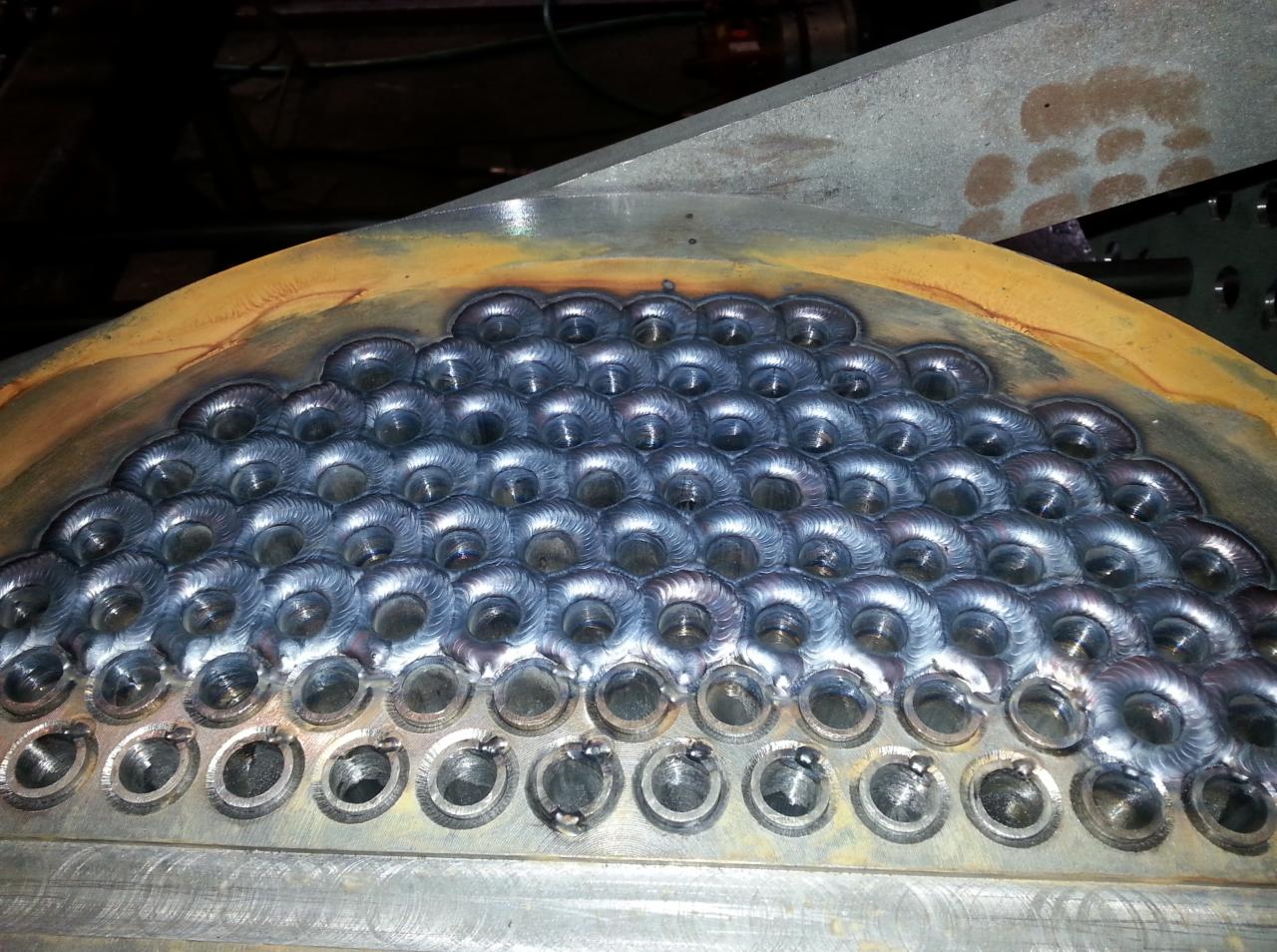 Fragment kotła z rzędami spawanych otworów, widoczne ślady obróbki i przebarwienia termiczne na metalu.