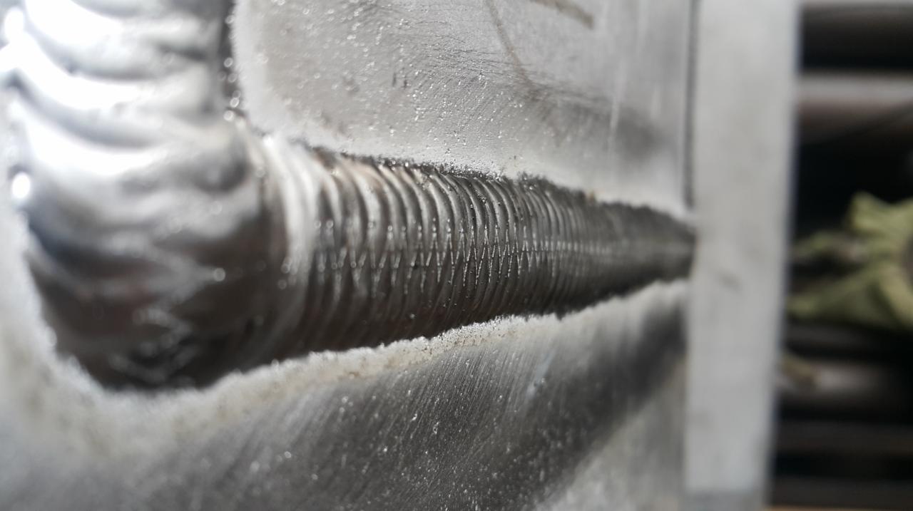 Szlifowana spoina na metalowej powierzchni, widoczne regularne ślady po spawaniu, oświetlenie studyjne.