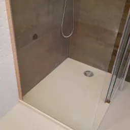 Nowoczesny brodzik z kabiną prysznicową i armaturą w odcieniach brązu, widok z góry na odpływ.