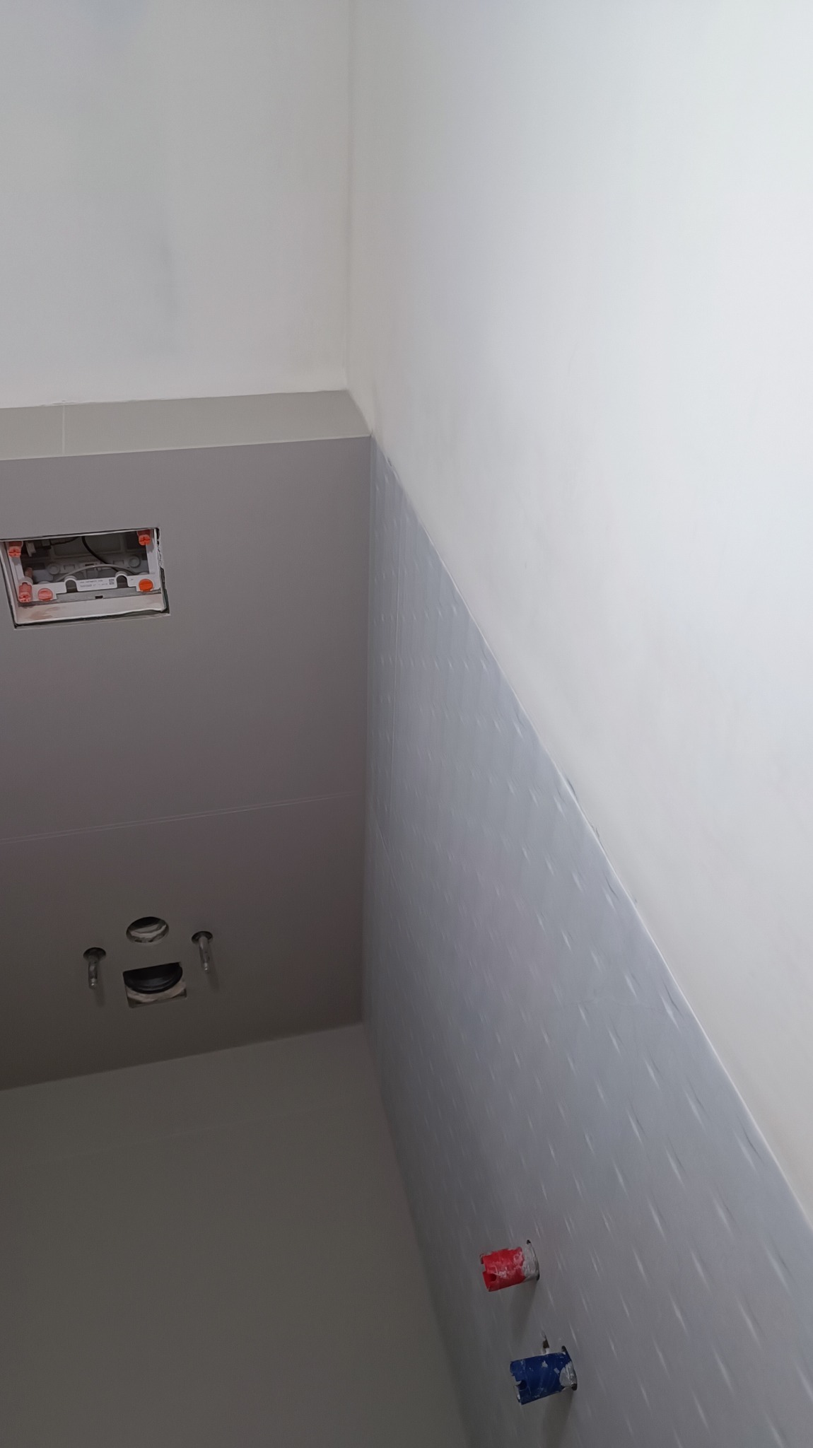 Świeżo wykończona ściana w łazience z zamontowanymi gniazdami instalacyjnymi, widoczna instalacja podtynkowa i przygotowane przyłącza wodne z zaślepkami.