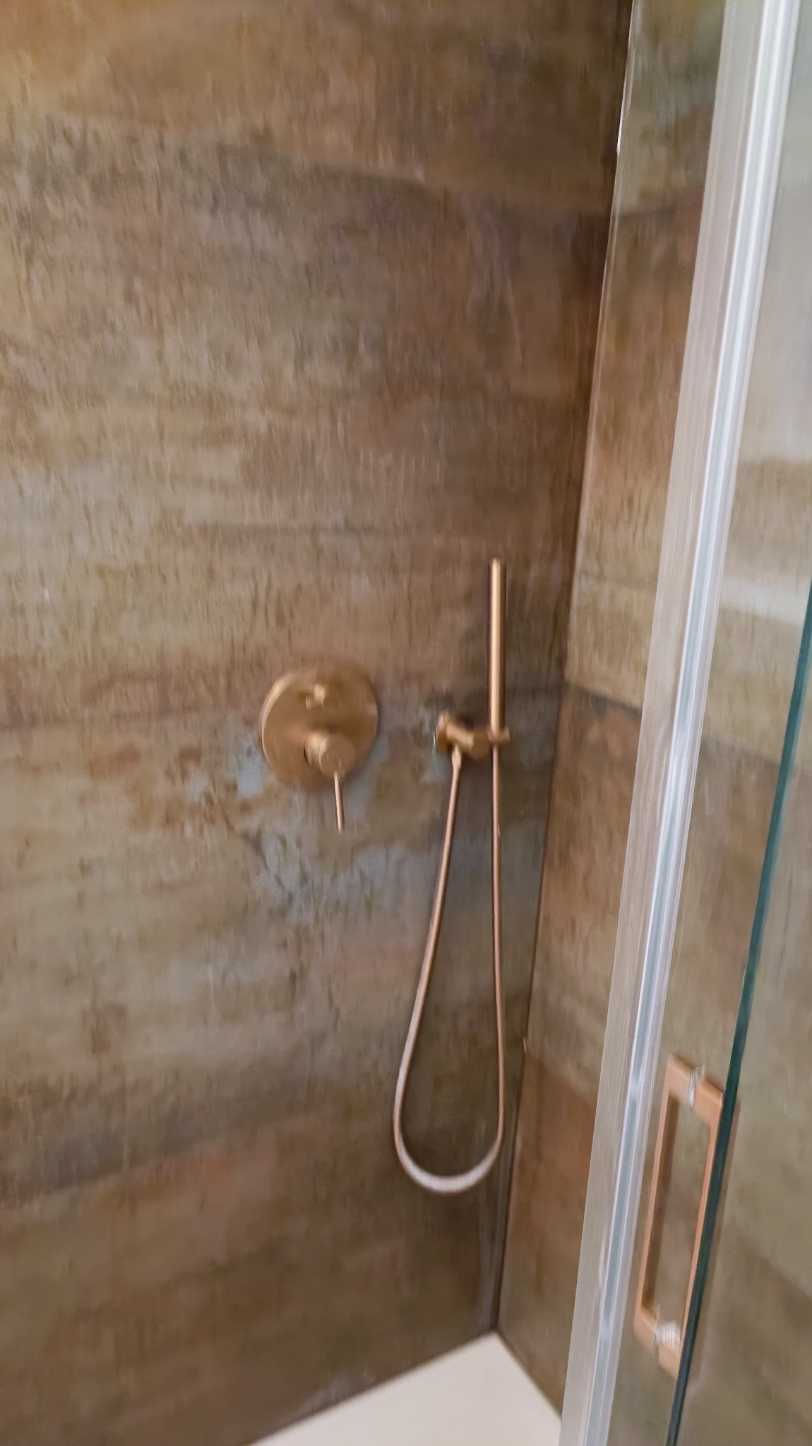 Kabina prysznicowa z panelami imitującymi rdzę i złotą armaturą, widoczny szklany panel z uchwytem