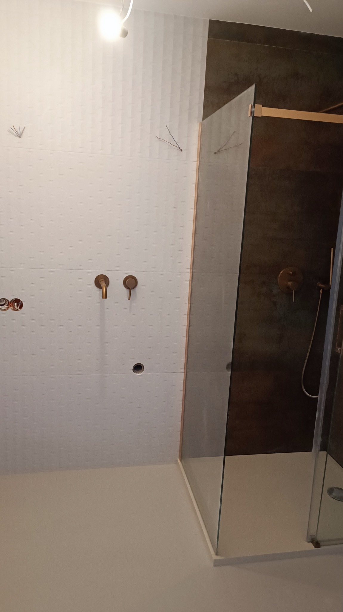 Nowoczesna kabina prysznicowa z brązowymi armaturami i białymi, teksturowanymi płytkami w łazience w Namysłowie, w trakcie montażu.